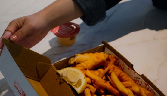 Hand opening box of fish and chips with lemon
